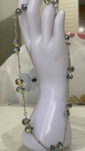 Silver chain necklace with iridescent blue and yellow beads draped over white mannequin hand.