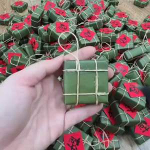 Liễn treo bánh trưng bánh tày mô hình màu xanh lá cây với tua rua đỏ và chữ "Tết" đỏ treo mai đào