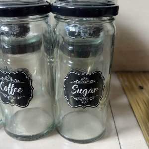 Glass jars with black lids labeled Sugar Creamer Coffee for kitchen storage.