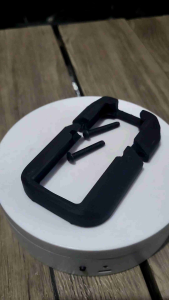 3D printed toy decoration M4/AR magwell for softair toys and gel blaster. Black plastic magwell with two screws. Fits M4/AR style softair guns. Displayed on a white circular surface.