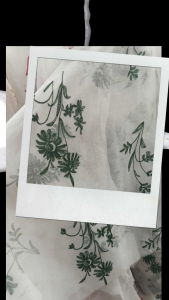 White sheer fabric with green floral embroidery. Lightweight and delicate suitable for summer garments. Ideal for dresses or scarves.