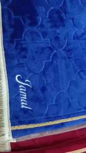 Brown embroidered prayer mat with name "Yusmin" and decorative tassels.