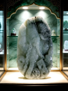 Jade carving with deity figure intricate details smooth texture green and white hues displayed in glass case.