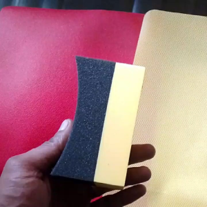 Black and yellow foam cleaning sponge with curved top for car detailing.