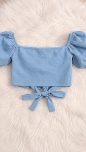 Blue off-shoulder crop top with puff sleeves and lace-up back paired with high-waisted wide-leg jeans.