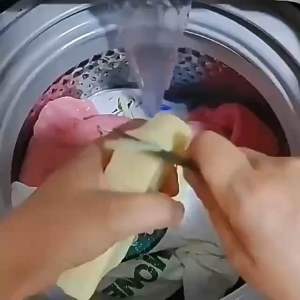 White bar soap with blue label. Wooden tub with soap suds. Clothesline with hanging shirts. Outdoor scene with grass and trees sabun penghilang kotoran kulat bau hitam