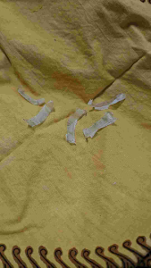 Transparent plastic strip on yellow fabric. Thin elongated slightly curved with visible texture and edges. Suitable for crafting or repair purposes. Displayed on a soft textured surface.