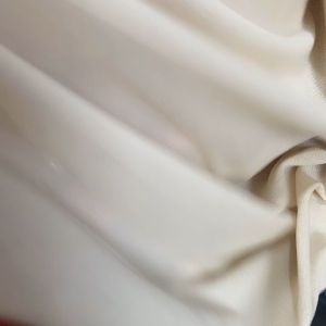 Cream-colored lightweight fabric draped elegantly. Soft texture and smooth flow. Suitable for casual or formal wear. Ideal for warm weather or layering.