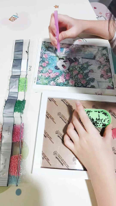 Diamond painting kit featuring a white cat with pink cheeks sitting on a windowsill surrounded by pink flowers and green leaves. Made in China.