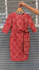 ชุดผ้าไทยสีแดง ผ้าฝ้ายทอลายแพรวากาฬสินธุ์ ออกแบบคอกลม แขนสามส่วน แต่งเอวป้ายหางโบว์ งานอัดกาว กระโปรงทรงสอบ มีกระเป๋าข้าง