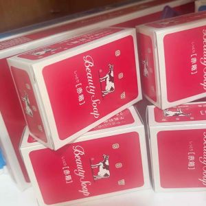Beauty Soap with cow logo red packaging boxes on white surface with decorative items in background.