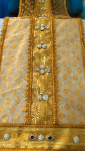 ผ้าสไบห่มพระ หน้าตัก65"-65"กว้าง40ซม. ยาว 3 เมตร ทำจากผ้าสีทองลายเลื่อมดอกมะลิเกรดพรีเมี่ยม มีความระยิบระยับตา และดิ้นทอง2ชั้น ไม่มีซับ ด้านหน้าประดับด้วยมุกสีขาวและคริสตัลสีเขียวและขาว ด้านหลังเป็นดอกไม้สีขาวเล็กๆ  เป็นงานฝีมือ