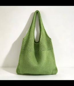 Knitted crochet tote bag with open weave design and solid bottom. Worn over shoulder with casual outfit.
