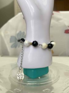 Black and white beaded bracelet with silver leaf charm on chain.