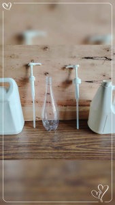 White plastic jugs with pump dispensers and clear glass bottle on wooden surface.