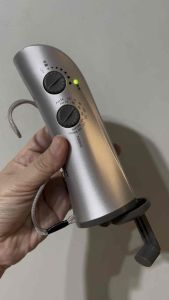 Silver handheld device with two dials and indicator lights. Adjustable settings for temperature and timer. Suitable for personal grooming or skincare routines.