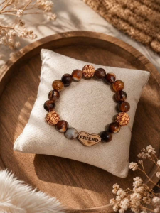 Wooden beaded bracelet with heart charm engraved FRIEND. Natural brown and amber tones. Displayed on cushioned pillow.
