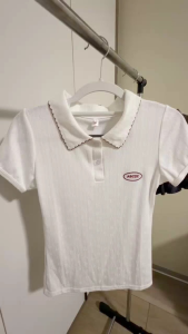 White polo shirt with red trim and pink bow detail paired with black pleated skirt.