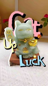 Green jade lucky cat figurine with gold accents holding a gold ingot and scroll on wooden base.
