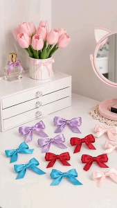 Colorful satin ribbon bows in purple blue red and pink for hair accessories or decoration on a white vanity table with a pink mirror and decorative items.