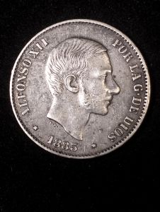 Silver coin featuring profile of Alfonso XII dated 1885 with inscription "POR LA G. DE DIOS" on black background. AU details preloved.