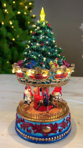 Christmas carousel music box with rotating horses and Santa figure featuring a decorated tree and star on top ornate blue and red base and mounted on a wooden surface.