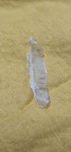 Transparent plastic strip on yellow fabric. Thin elongated slightly curved with visible texture and edges. Suitable for crafting or repair purposes. Displayed on a soft textured surface.