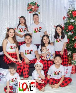 CHRISTMAS T-SHIRT AND PAJAMA TERNOS FAMILY SET - White T-shirts with festive text red plaid pajama pants suitable for family holiday photos set against Christmas decorations.