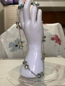 Silver chain necklace with iridescent blue and yellow beads draped over white mannequin hand.