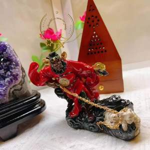 Red ceramic deity figurine with golden chain and white animal base.
