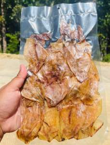 Dried squid snack in transparent plastic bag held in hand with outdoor background.