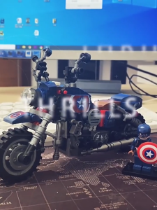 Captain America themed block motorcycle toy with star emblem and chrome details. Bricks minifigure with shield stands beside it.
