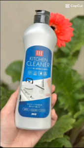 Nước rửa chén IH Kitchen Cleaner chai nhựa trắng nhãn xanh dương hình ảnh dụng cụ nhà bếp tay cầm chai nền cây xanh và hoa đỏ.