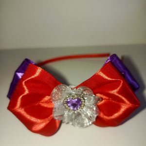 Pink and blue satin bow headband with rhinestone flower centerpiece. Suitable for young girls. Outdoor setting.