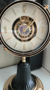 Antique-style mechanical desk clock with gold and black finish. Visible gears Roman numerals and ornate design. Suitable for office or home decor.