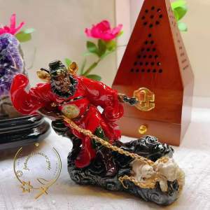 Red ceramic deity figurine with golden chain and white animal base.