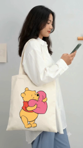Canvas tote bag featuring Winnie the Pooh Tigger Eeyore and Piglet characters. Casual everyday use. Indoor setting.