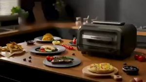 Hamilton Beach AirGrill Air Fryer and Grill AF06201 with digital control panel sleek black design placed on wooden countertop with cooked steak vegetables and fries.