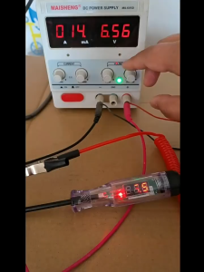 Digital Display Vehicle Measuring Pen with Red Coiled Cable and Clip. Positive and Negative Electrode Indicators. Automotive Repair Scene.