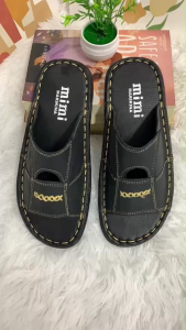 K89 Black slip-on sandals with white stitching and gold lettering on a fluffy white surface.