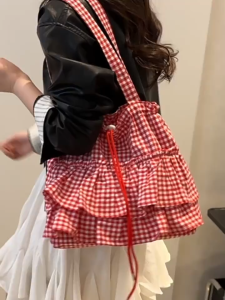 กระเป๋าทรงถุงใบใหญ่ มีสไตล์ที่โดดเด่น จุดเด่นอยู่ที่ลายตาราง Gingham Check สีสดใส และดีเทลระบาย ขนาดใหญ่ที่ขอบกระเป๋า ทำให้มีลุคแบบ Cottagecore Retro Cute หรือ Y2K Sweet