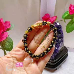 Rose quartz bracelet with gold accents in a white container. Pink beads gold charms decorative setting.