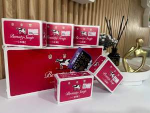 Beauty Soap with cow logo red packaging boxes on white surface with decorative items in background.