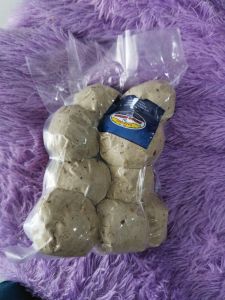 Bakso Ikan Besar Isi 10 Bijian dalam Kemasan Plastik Transparan dengan Label Biru di Atas Permukaan Berbulu Ungu