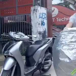 Bảo vệ xe máy bạc chống nước với các đặc điểm nổi bật như phản quang và thiết kế vừa vặn được đặt trên vỉa hè trước một tòa nhà.