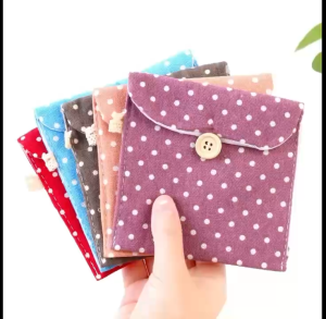 Polka dot fabric pouches with wooden button closures. Blue purple and pink pouches. One pouch open revealing sanitary pads inside.