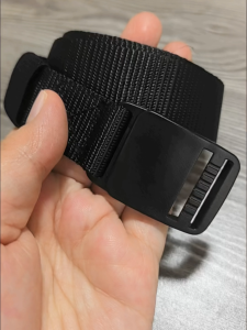 Black nylon belt with plastic buckle for casual wear. Adjustable strap with reinforced stitching. Suitable for everyday use.