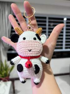 crocheted cow amigurumi which is a small stuffed yarn toy. It appears to be handmade and could be used as a keychain or decorative item