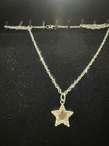 Silver necklace with flower pendant on black mannequin hand.