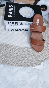 Brown and black two-strap flat sandals with beige option. Brown stitching on straps. Metal stud detail on black strap. Flat sole. Casual wear. Displayed on textured surface.